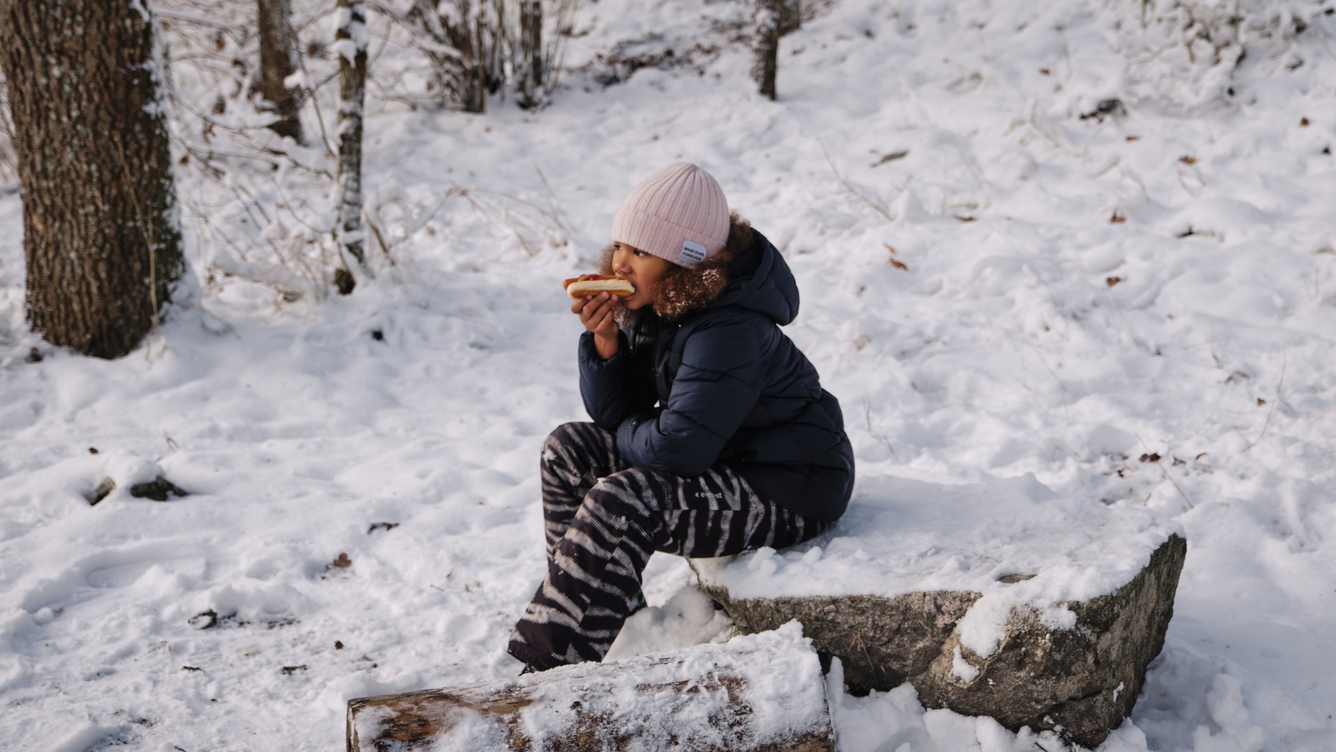 Flicka som äter korv och bröd i vintrig natur