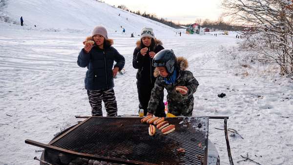 Tre barn grillar korv nedanför skidbacke