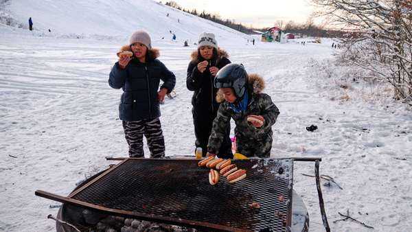 Three kids grilling hotdogs below the ski slope